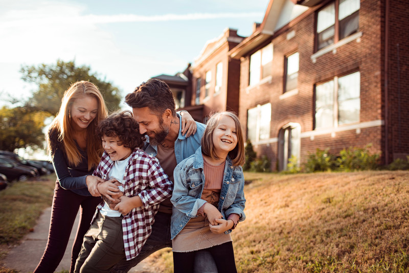 Mutter, Vater und Kind steht albernd vor einem Haus