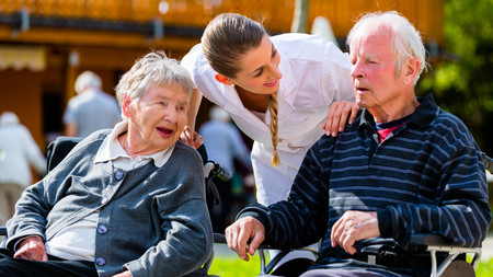 Zwei ältere Herren lachend im Rollstuhl mit einer Pflegerin sprechend