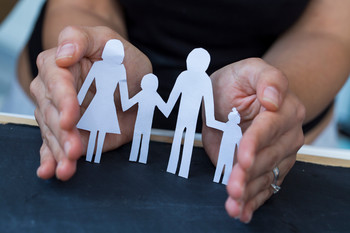 Hände, die ein Haus aus Papier umfassen