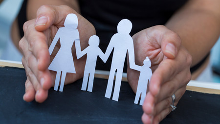 Hände, die ein Haus aus Papier umfassen