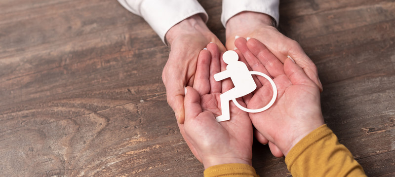 Vier Hände umfassen ein Papierschnitt (Rollstuhl)