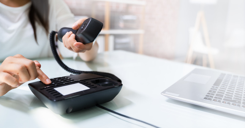 Eine Hand wählt eine Nummer auf ein Telefon