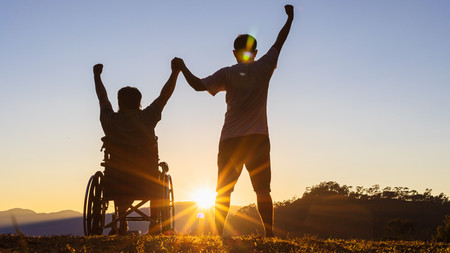 Rollstuhlfahrer mit Begleiter genießen den Sonnenuntergang