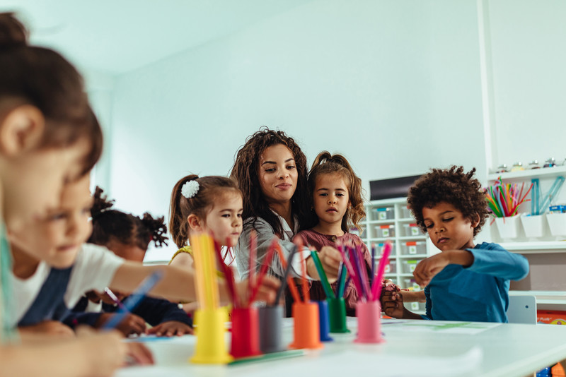 Erzieherin malt mit Kindern am Tisch
