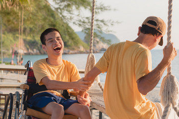 Junger Mann im Rollstuhl unterhalten sich lachend am See