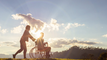 Betreuer schaut sich mit einem Rollstuhlfahrer den Sonnenuntergang an