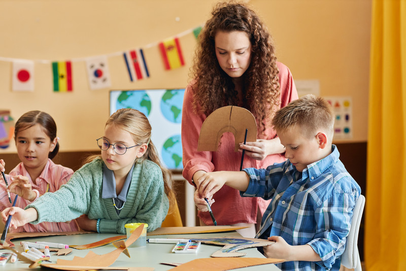 Kinder sitzen am Tisch und malen, die Betreuerin gibt Unterstützung