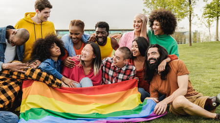 Gruppe von Jugendlichen, auf der Wiese sitzend mit einer Regenbogenfahne