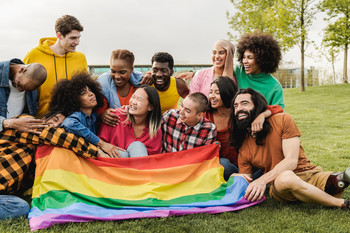 Gruppe von Jugendlichen, auf der Wiese sitzend mit einer Regenbogenfahne