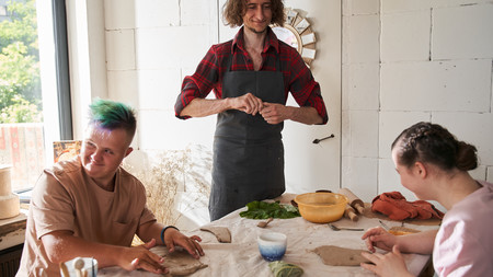 Mensch mit Behinderung sitzt lernend am Tisch, neben Ihm ein Lehrer
