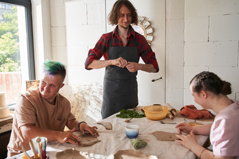 Mensch mit Behinderung sitzt lernend am Tisch, neben Ihm ein Lehrer