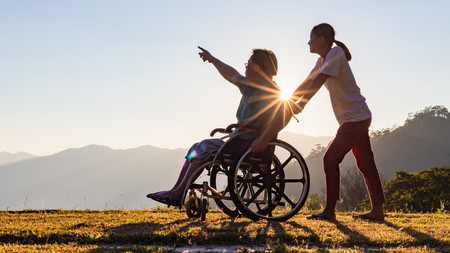 Mann im Rollstuhl geht mit Betreuerin spazieren